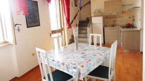 Un comedor con una mesa preparada para dos, una cocina al fondo y una escalera que sube.