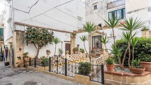 A narrow street with a white building featuring a stone facade, a wrought iron gate, and potted plants. - Palazzo Raheli (Gallipoli)