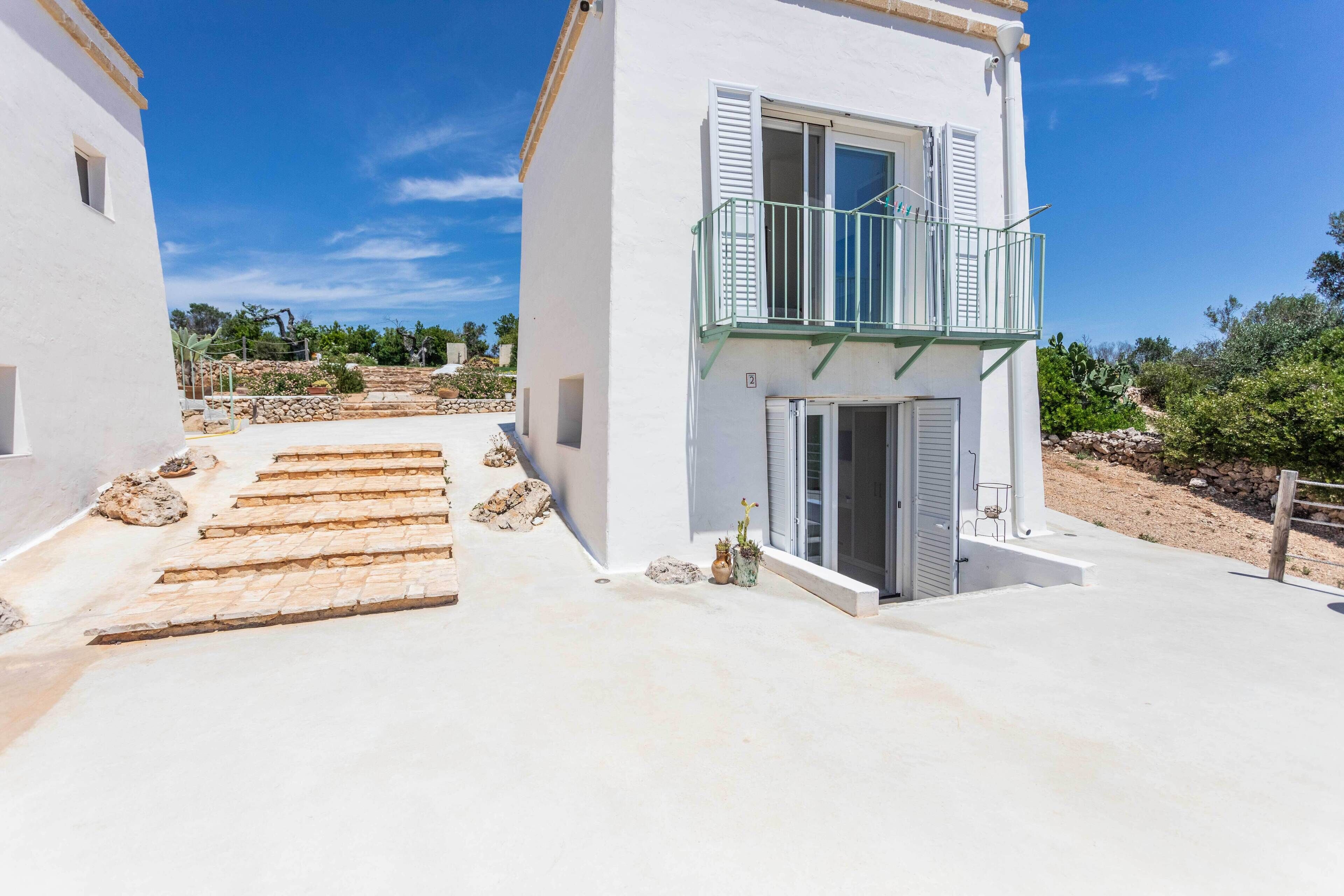 A modern white building with a balcony, steps leading to the entrance, and a clear sky.