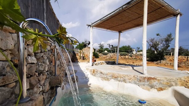 Un espace piscine agrémenté d’un mur en pierre, d’une pergola et d’une piscine à l’eau d’un bleu limpide.