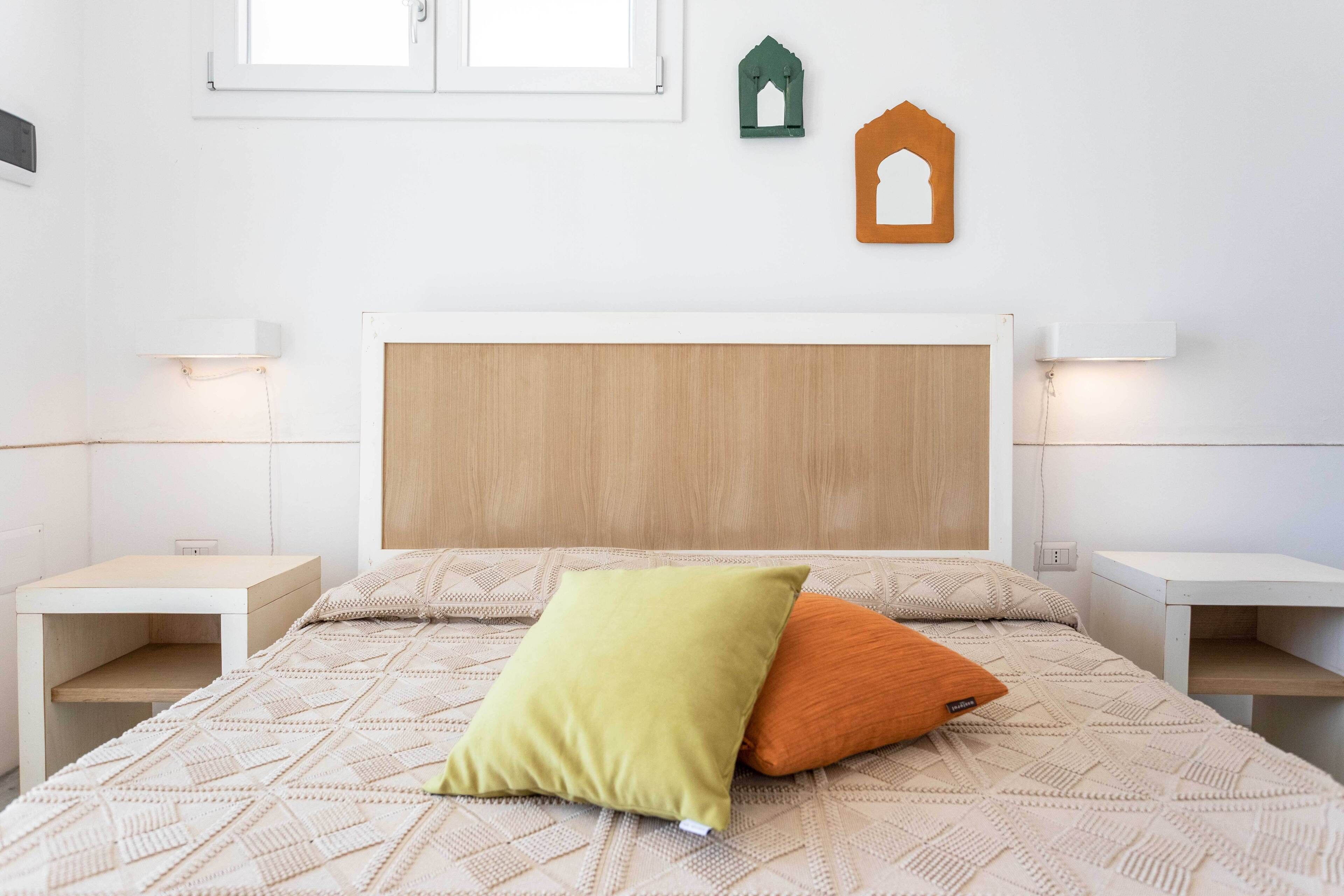 A neatly arranged bedroom with a wooden headboard, two bedside tables, and a bed with a patterned bedspread.