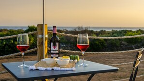 Une table avec deux verres de vin rouge, une bouteille de vin, des plats remplis de nourriture et une vue sur la mer.