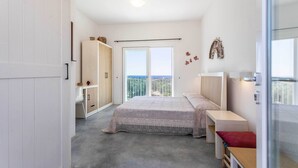 Une chambre avec un lit, un bureau, une armoire et un balcon offrant une vue.
