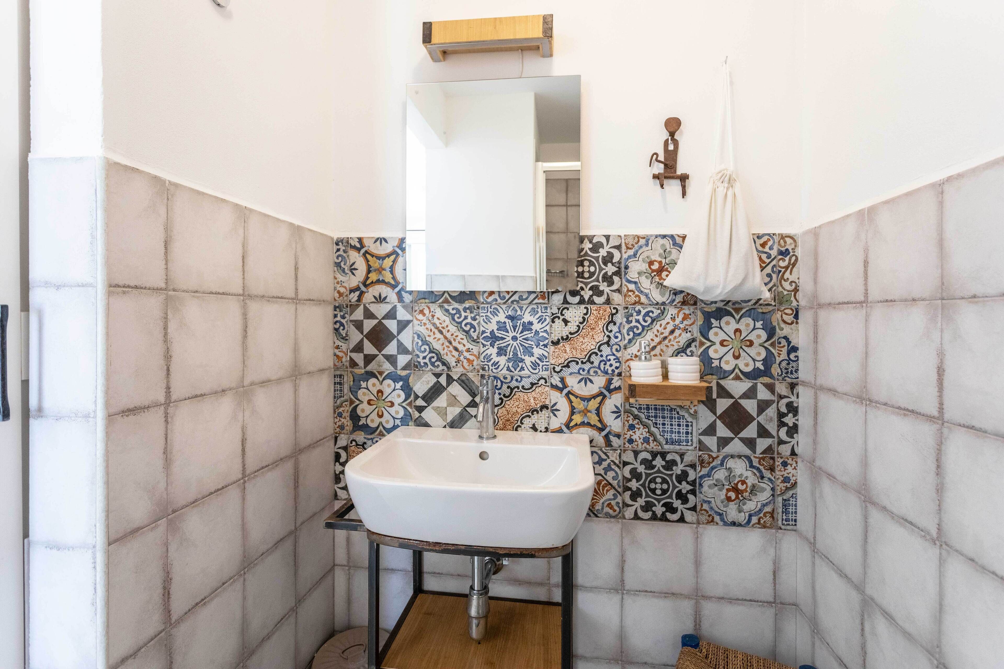 A bathroom with a white sink, tiled walls, and a wooden shelf.