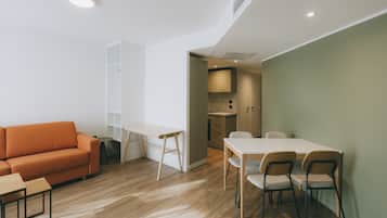 Una sala de estar moderna con un sofá, una mesa de comedor con sillas y una cocina visible a través de un umbral abierto.