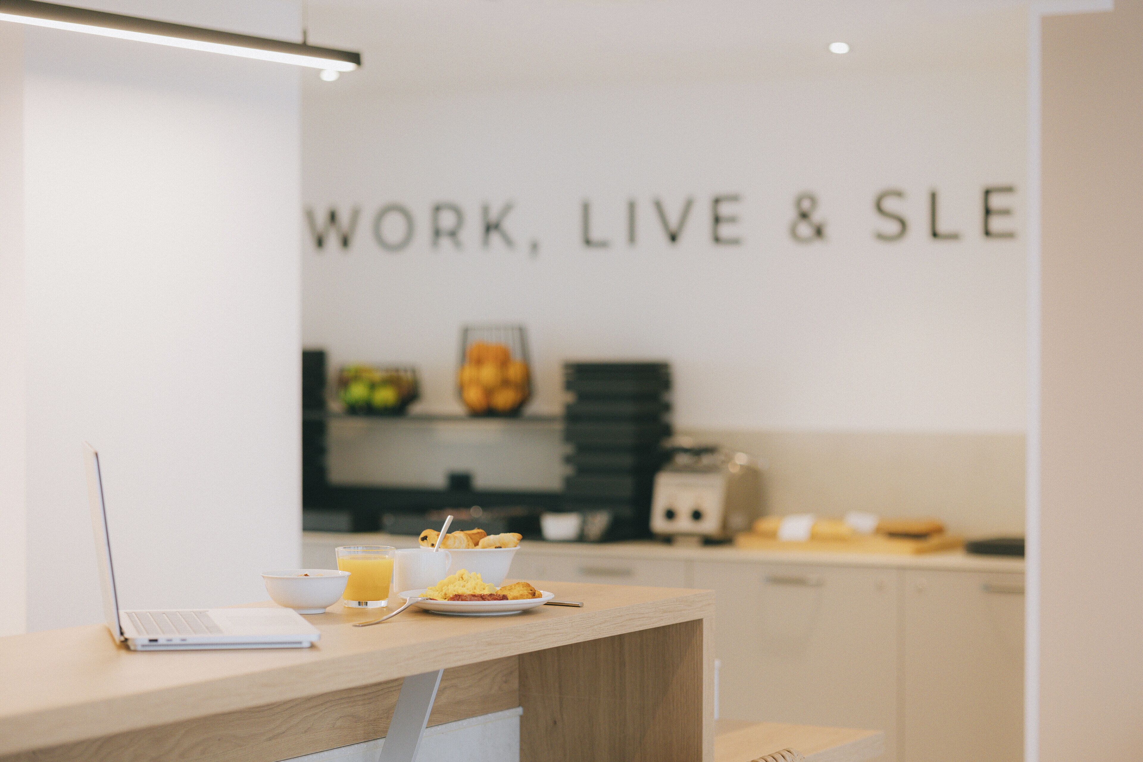 Una cocina moderna con una computadora portátil, alimentos para el desayuno y un letrero en la pared que dice "WORK, LIVE & SLE".
