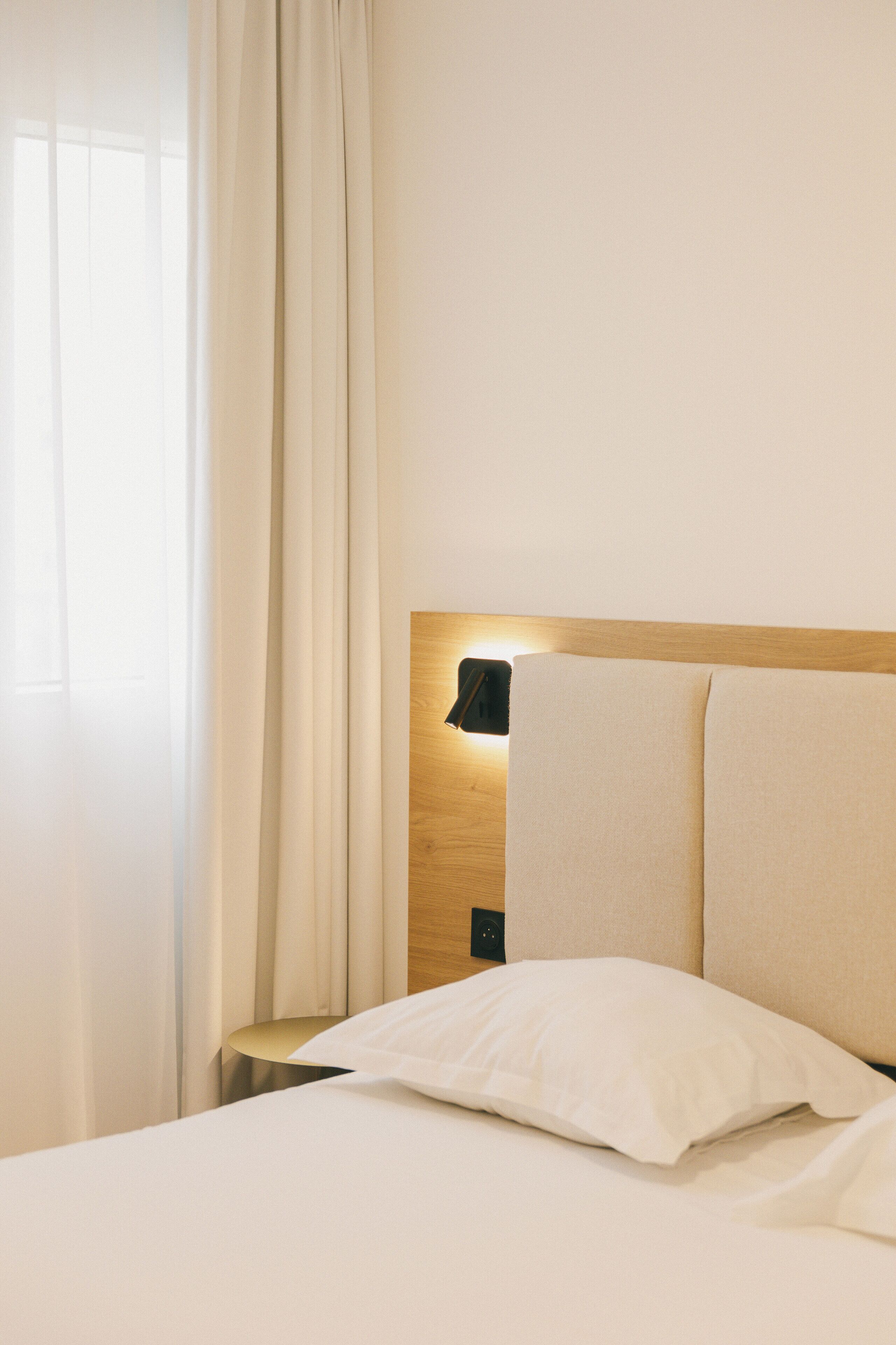 Une chambre d’hôtel avec un lit bien fait, une lampe de chevet et une fenêtre avec des rideaux.