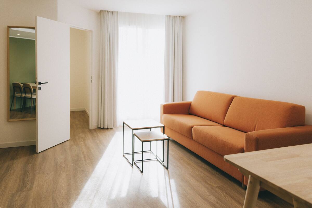 Un salon moderne avec un plancher en bois, un canapé orange, une petite table et un miroir au mur.