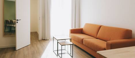 Una sala de estar moderna con suelo de madera, un sofá naranja, una mesita y un espejo en la pared.