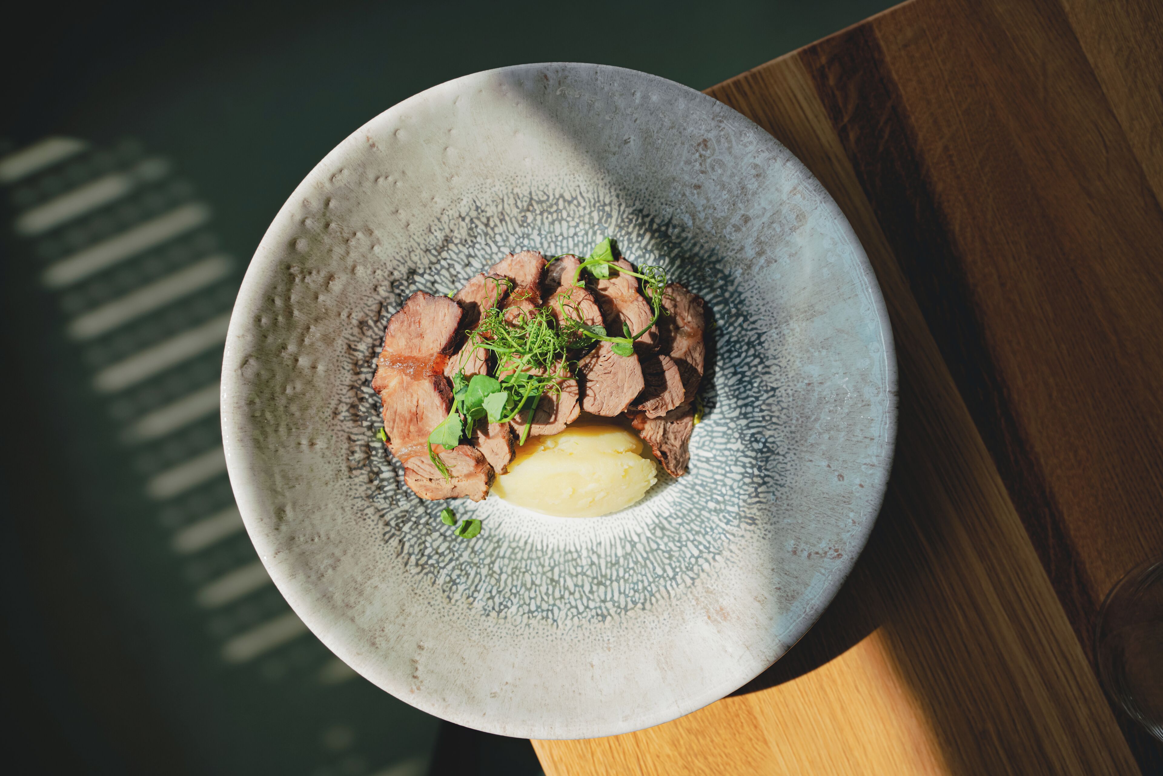 A plate of sliced meat with a pat of butter and greens on a textured ceramic plate.