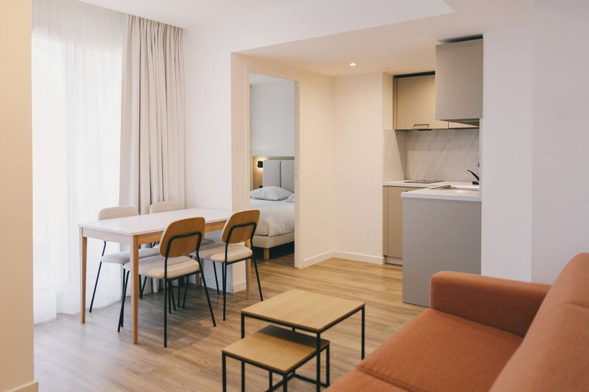 Un salon moderne avec un plancher en bois, une table à manger avec des chaises, un canapé et un coin cuisine équipé de placards et d’un plan de travail.