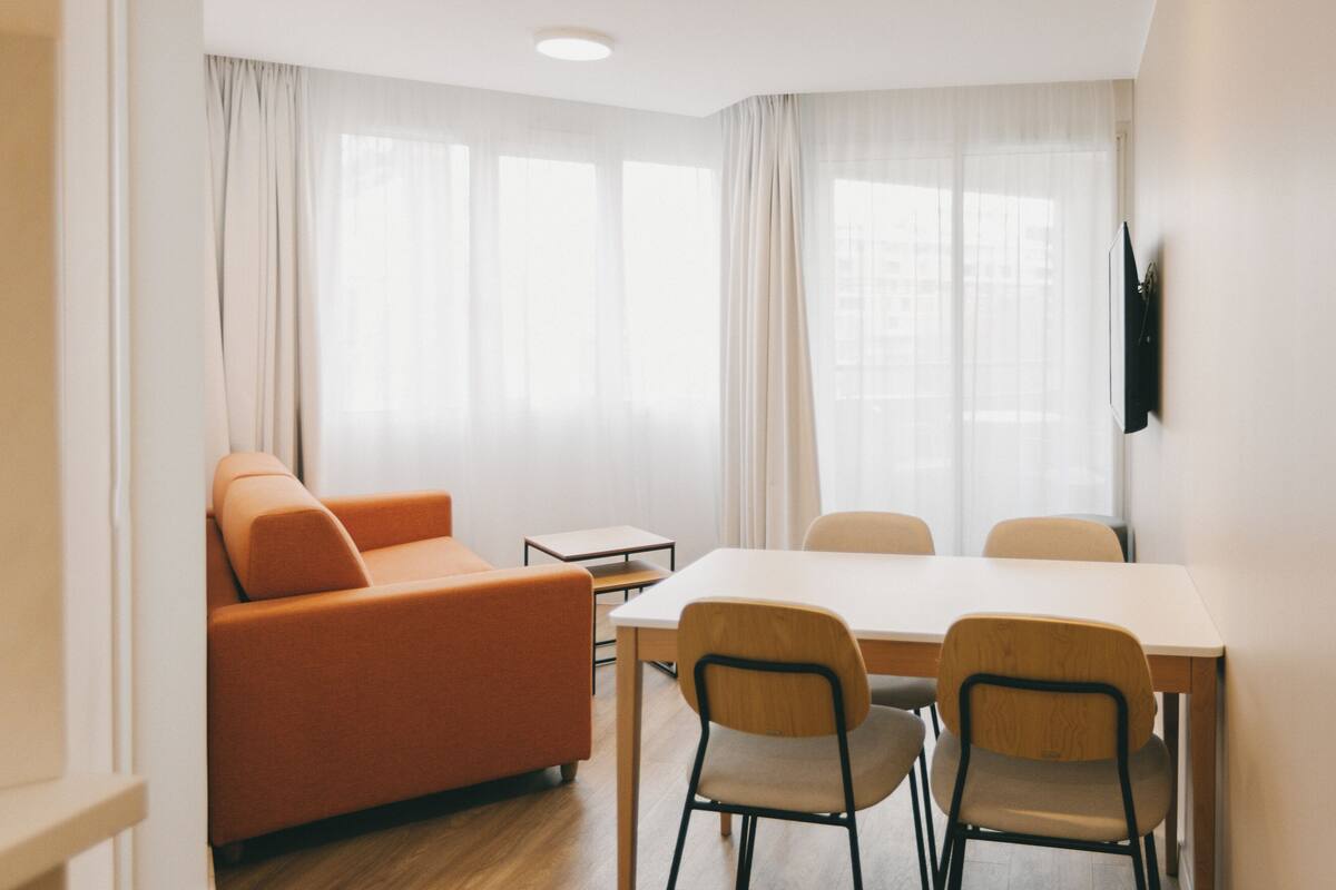 Une pièce moderne comprenant un canapé, une table à manger avec des chaises et un téléviseur à écran plat fixé au mur.