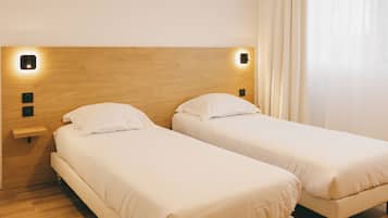 Hotellihuone, jossa on kaksi erillistä sänkyä, puiset päätylevyt, yöpöydät ja ikkuna, jossa on verhot.