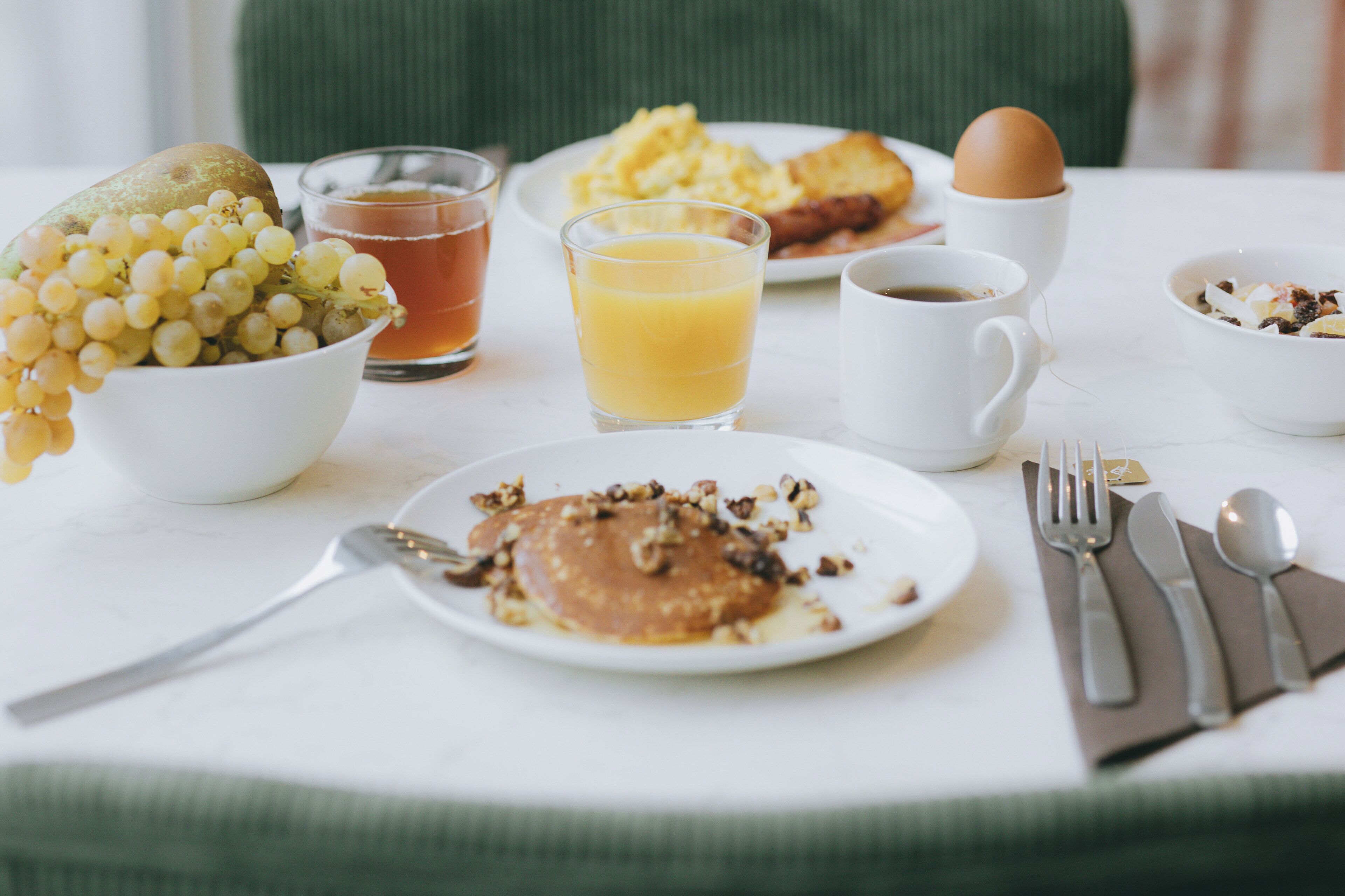 A breakfast table with a plate of pancakes, a bowl of grapes, a glass of orange juice, and a cup of coffee.