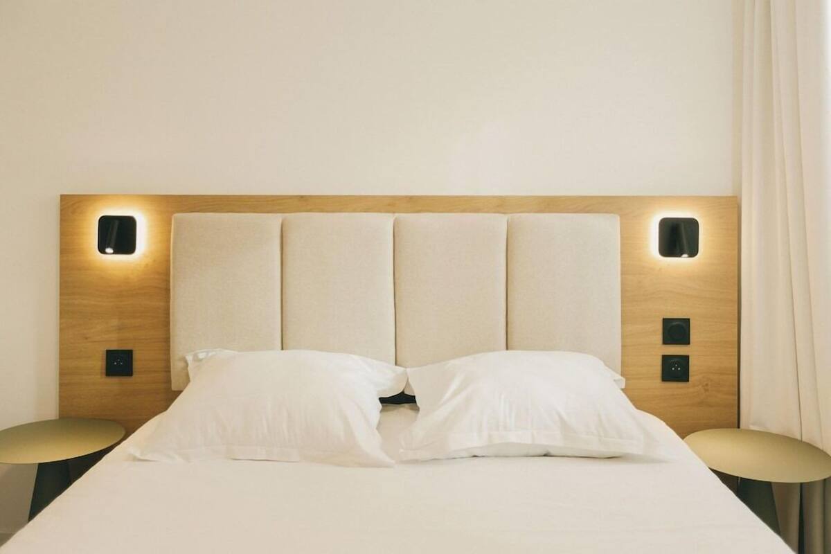 Une chambre d’hôtel comprenant un lit, deux tables de chevet et une tête de lit dotée d’un éclairage intégré.