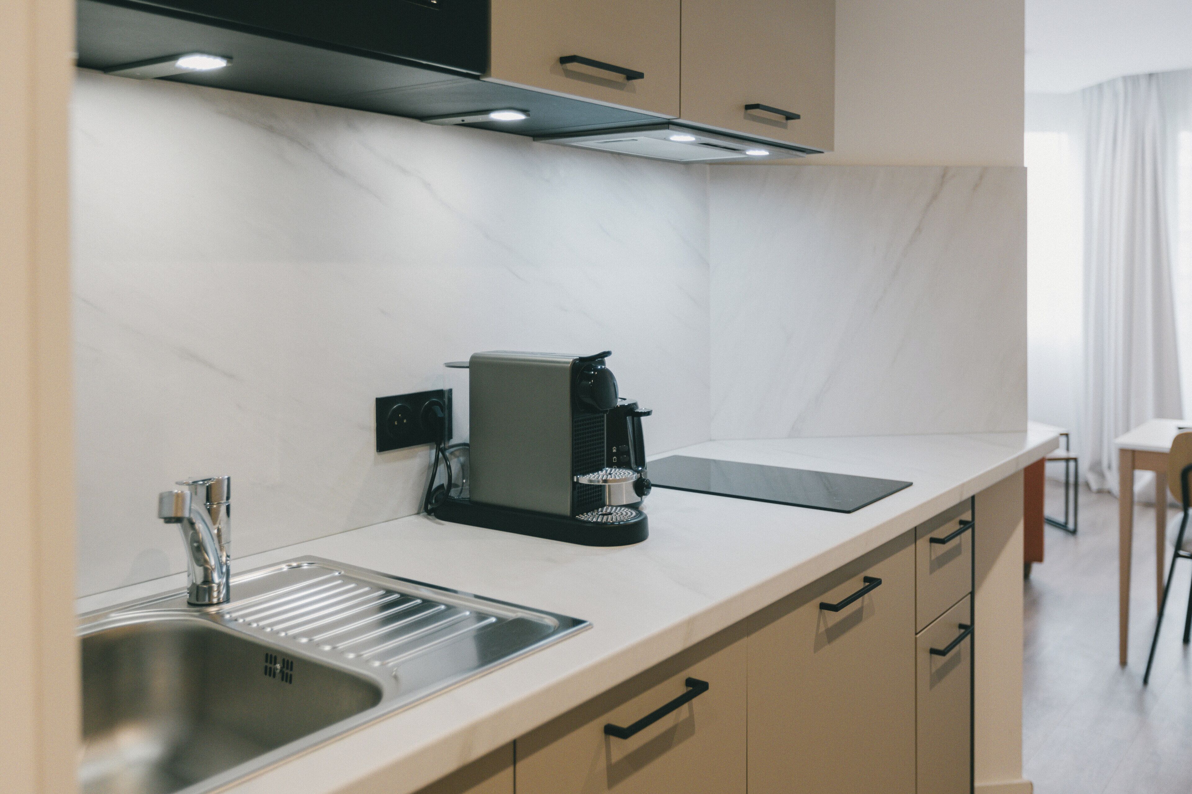 Una cocina moderna con cafetera espresso integrada, un lavamanos y una encimera.