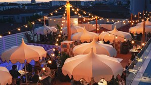 Un área de comedor al aire libre con varias mesas y sombrillas, rodeada de luces colgantes.