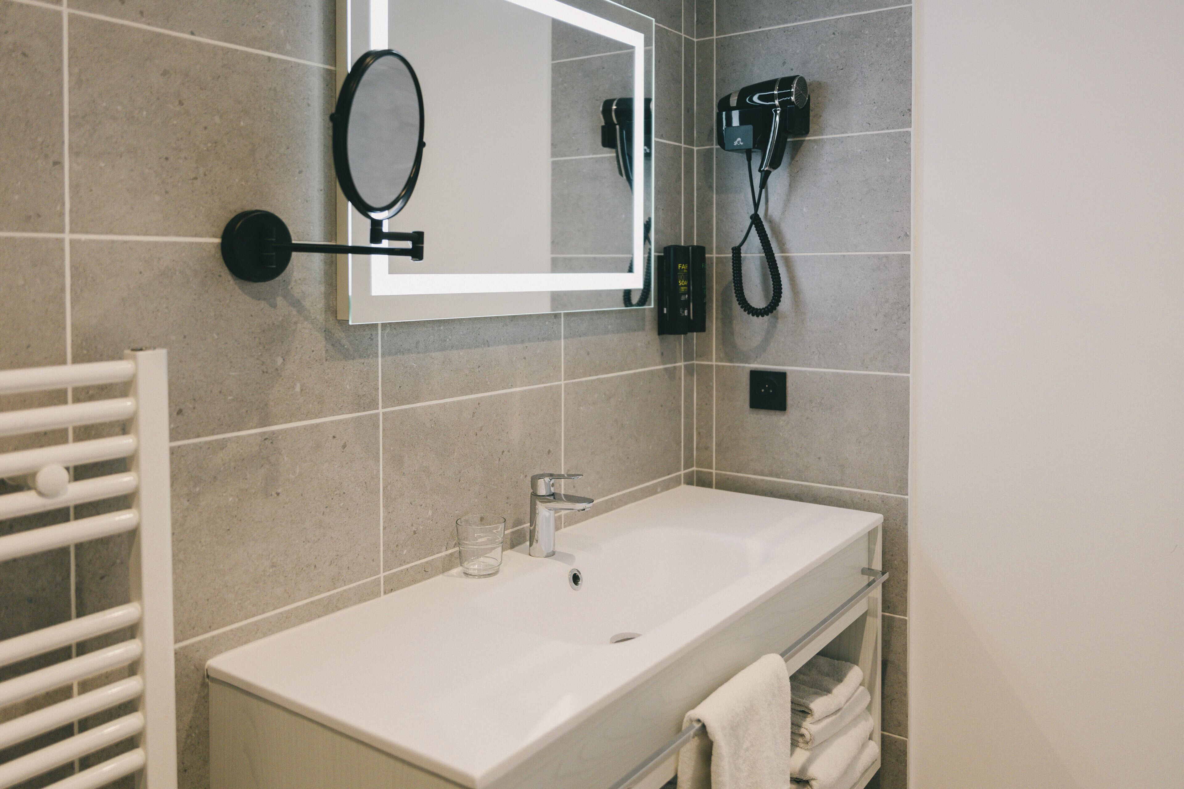 Une salle de bain avec un lavabo blanc, un miroir, un porte-serviettes et un sèche-cheveux fixé au mur.