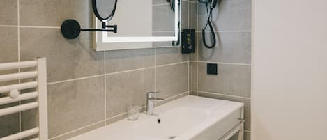 A bathroom with a white sink, a mirror, a towel rack, and a hairdryer mounted on the wall.