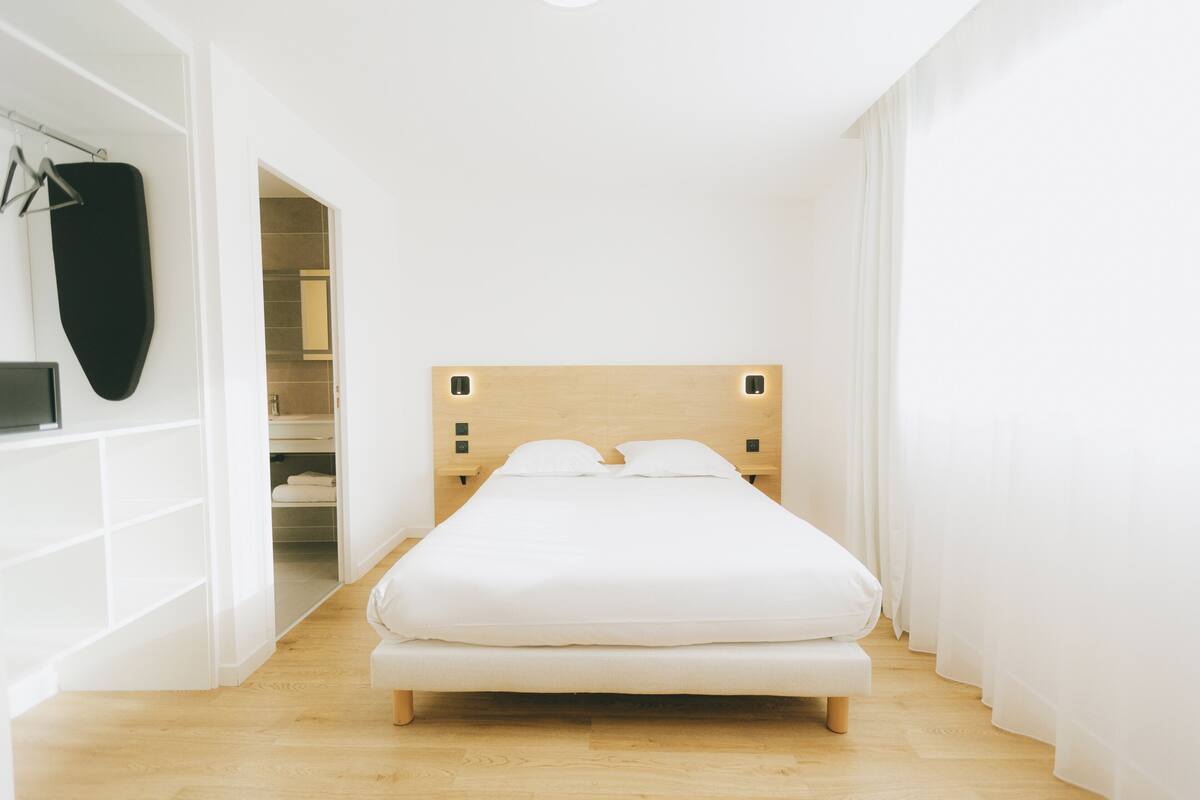 Une chambre à coucher au style minimaliste, avec une tête de lit en bois, un lit blanc et un dressing.