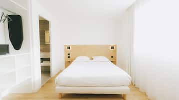 Een minimalistische slaapkamer met een houten hoofdbord, een wit bed en een inloopkast.