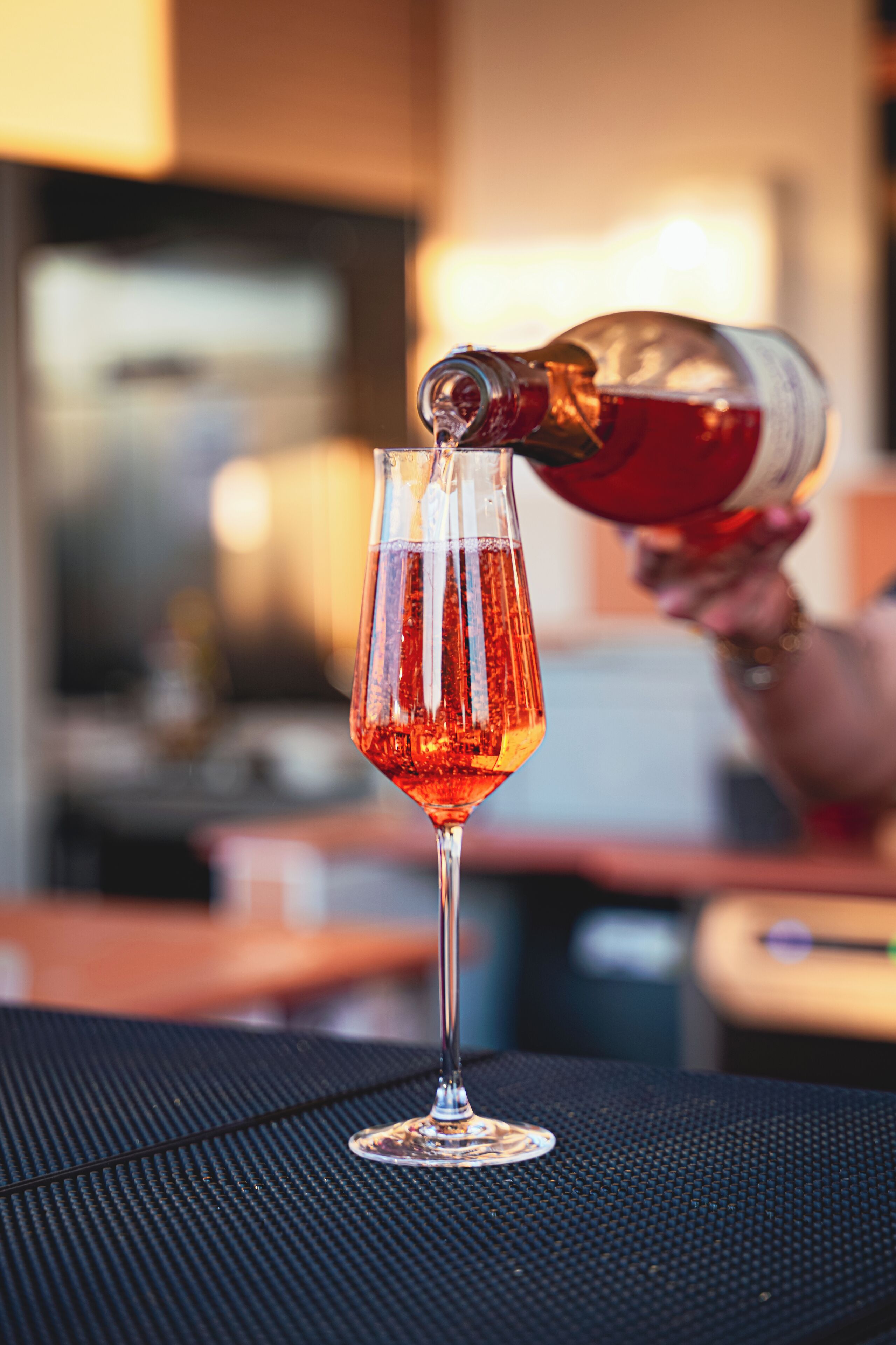 A glass being filled with a red liquid, likely a cocktail, on a table with a black textured surface.