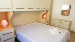 A bedroom with a bed, a bedside table with a lamp, a dresser, and a mirror on the wall. - VersoSud - Appartamento Colaianni 24 (Ugento)