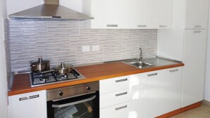 A kitchen with white cabinets, a stainless steel stove, and a tiled backsplash. - VersoSud - Appartamento Colaianni 24 (Ugento)