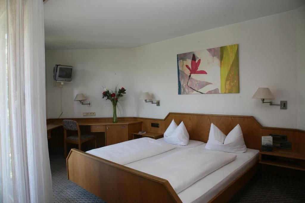 Una habitación de hotel con cama, escritorio, silla, televisor y obras de arte en la pared.