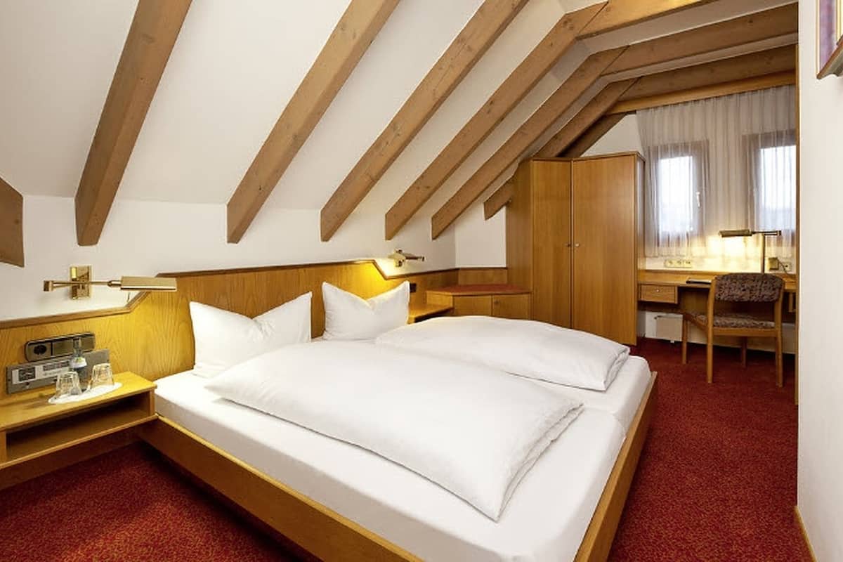 A hotel room with a large bed, wooden headboard, a desk with a chair, and a wardrobe.