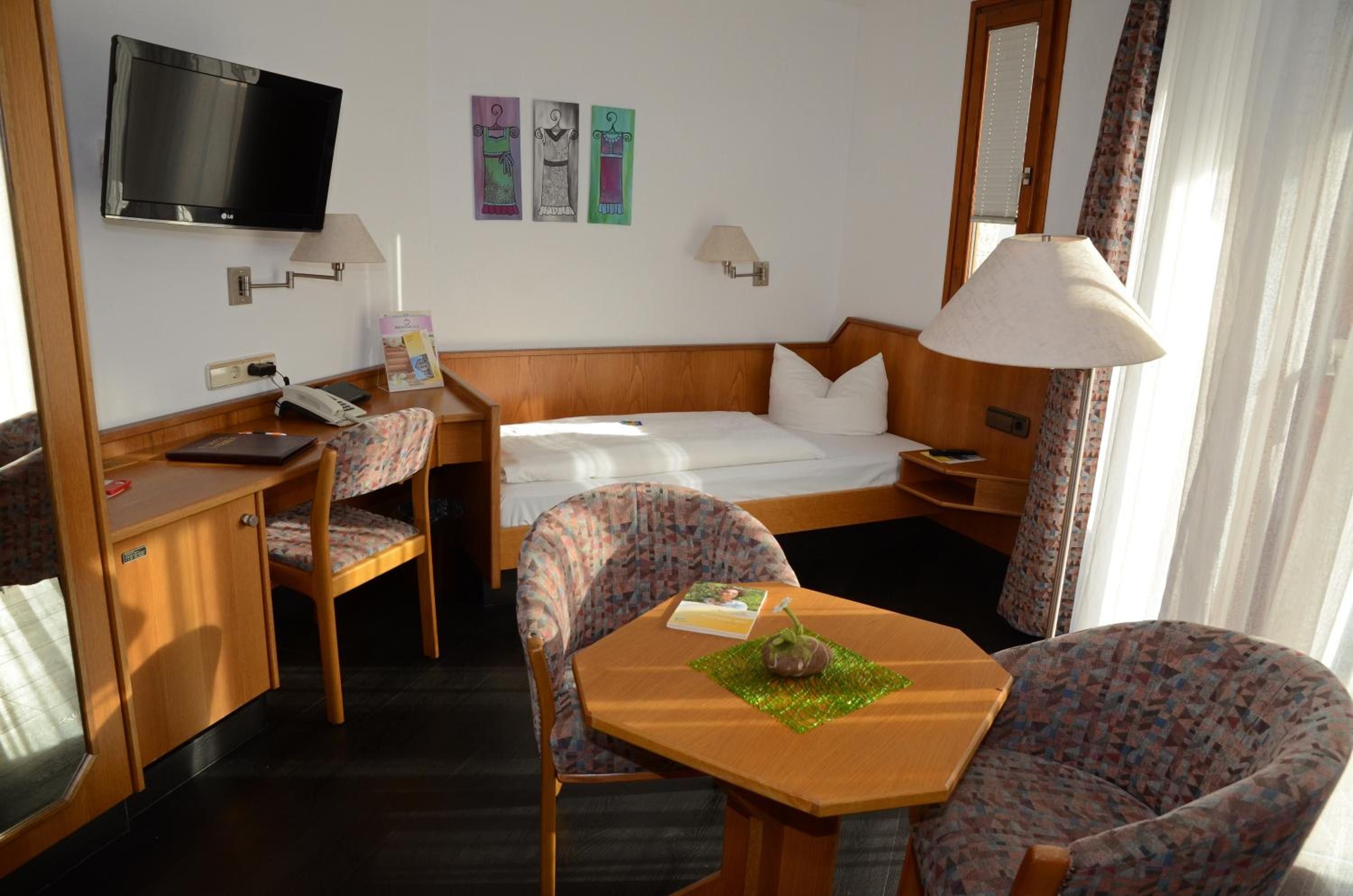 A hotel room with a bed, a desk, a chair, a table, a television, and a window with curtains.