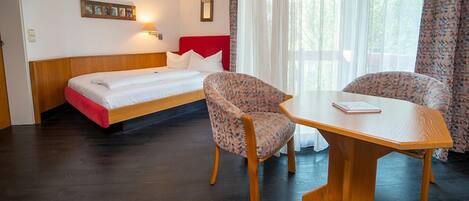 A hotel room with a bed, two chairs, a table, and a window with curtains.