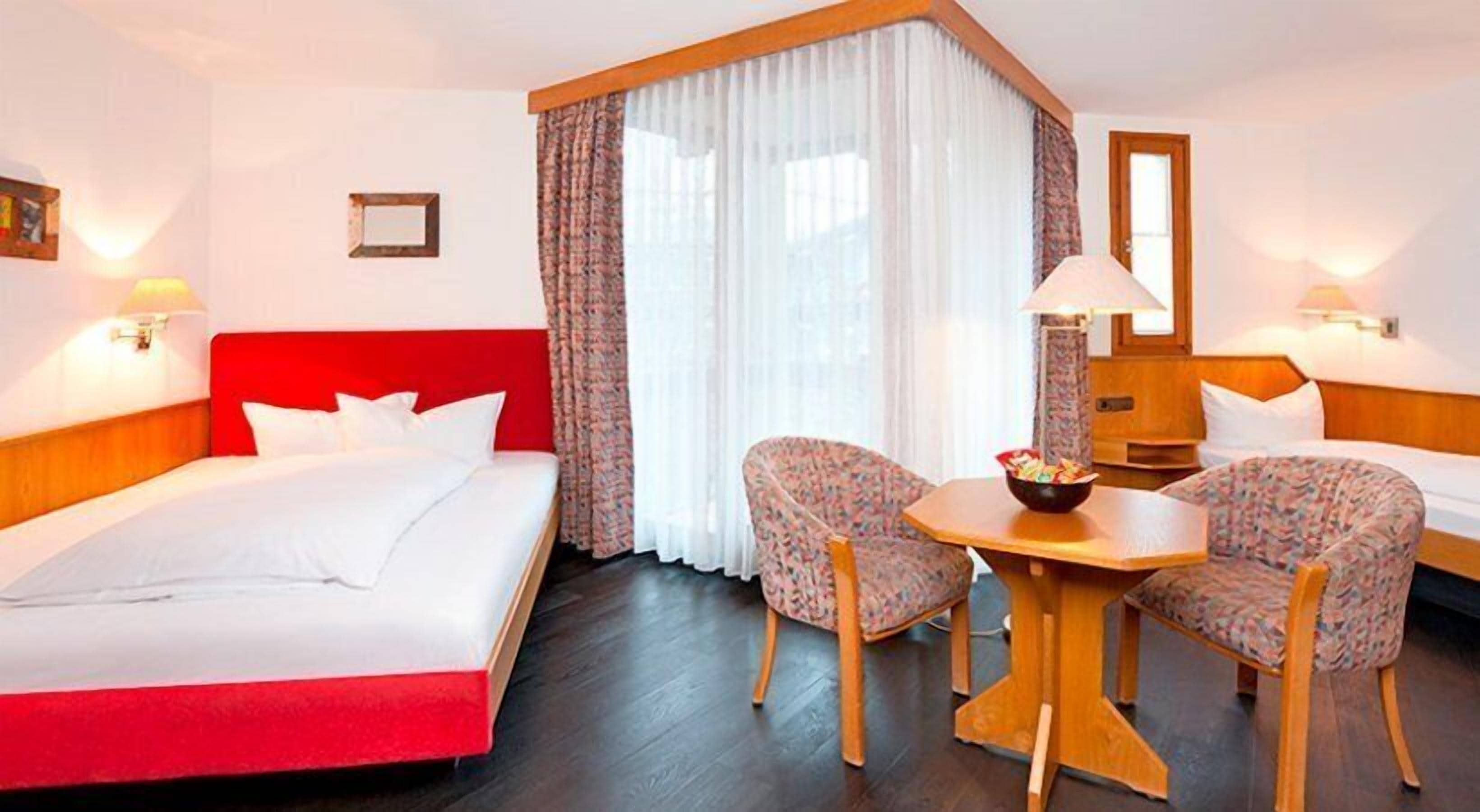 A hotel room with a bed, two chairs, a table, and a window with curtains.