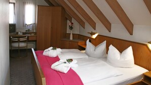 A hotel room with a wooden ceiling, a bed with white linens and pillows, a desk with a chair, and a small table with a vase of flowers.