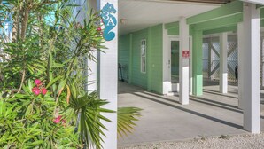 Un bâtiment à l’extérieur vert et à la porte blanche. Il y a une pancarte sur la porte qui indique : « Il est interdit de faire des fissures sous la maison. »