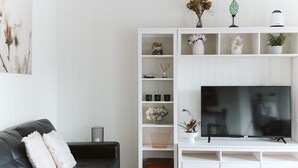 A modern living room with a black leather sofa, white shelving unit, and a flat-screen TV. - Possums Retreat - Private Spacious Cottage with Hydrotherapy Spa (North Maleny)