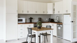 A modern kitchen with white cabinets, a wooden dining table, and black chairs. - Possums Retreat - Private Spacious Cottage with Hydrotherapy Spa (North Maleny)