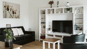 A modern living room with a black sofa, a coffee table, and a TV on a white entertainment unit. - Possums Retreat - Private Spacious Cottage with Hydrotherapy Spa (North Maleny)