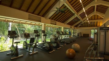 A gym with exercise equipment, large windows, and a high ceiling.