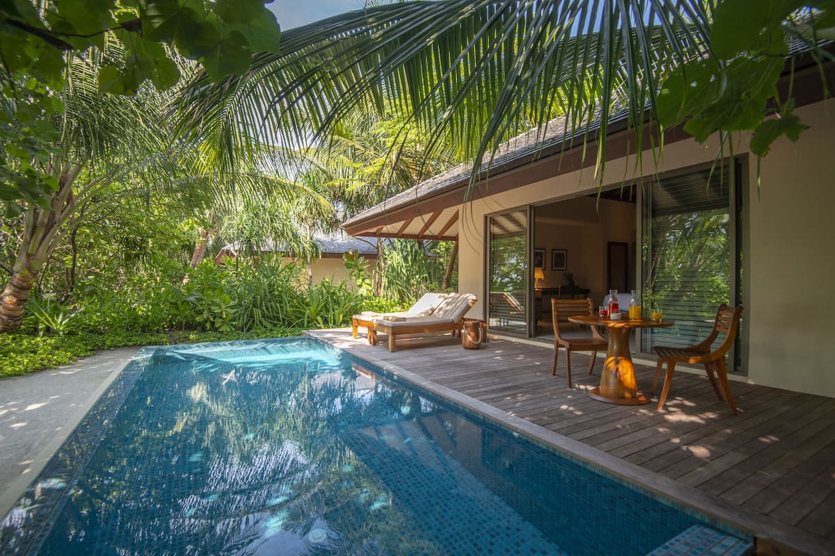 A swimming pool with wooden deck and lounge chairs, surrounded by lush greenery.