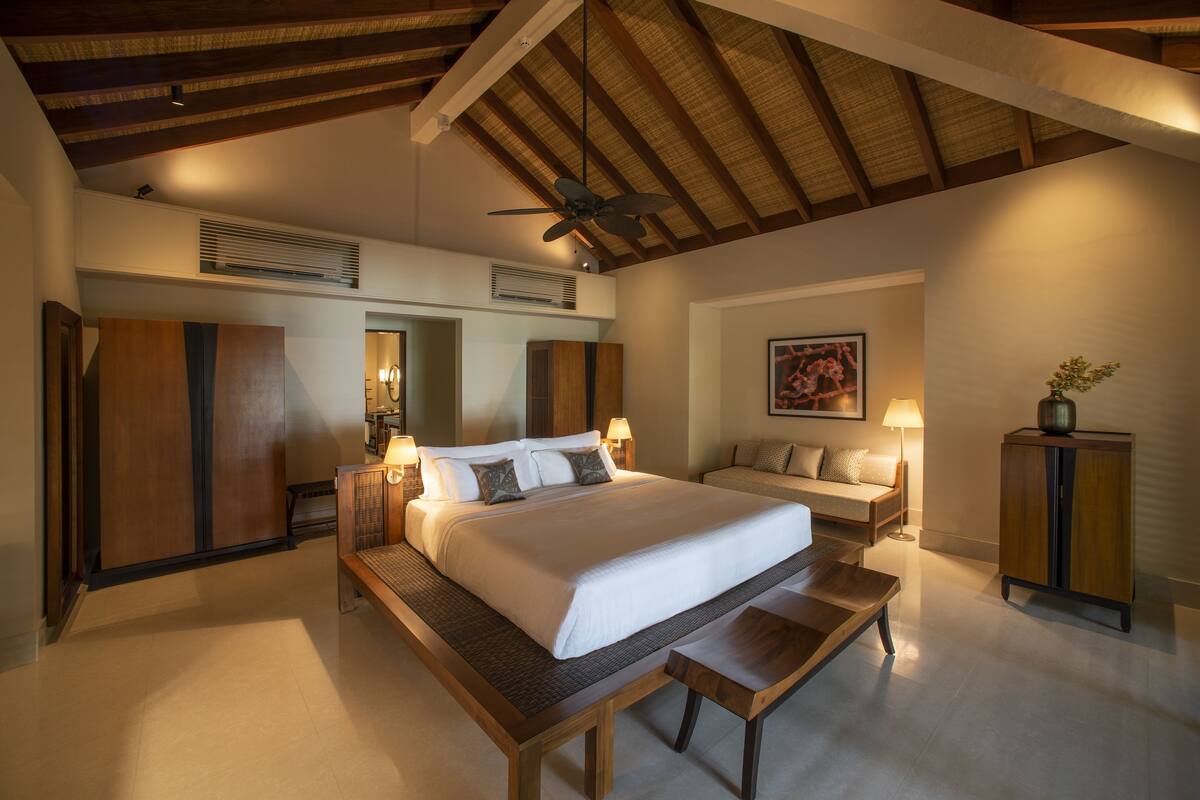 A spacious bedroom with a large bed, a wooden bench, a desk, and a ceiling fan.