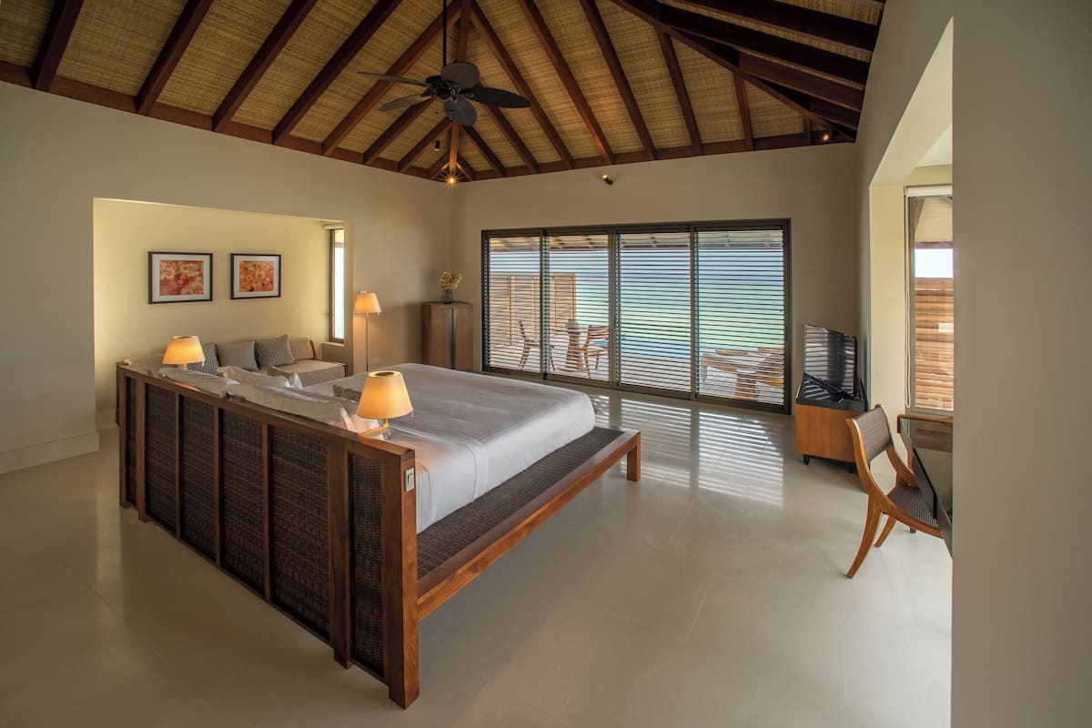 A spacious bedroom with a large bed, a ceiling fan, and a view of the outdoors through large windows.