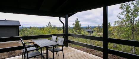 A wooden deck with a table and chairs, overlooking a forested area.