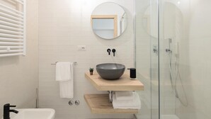 A modern bathroom with a glass shower enclosure, a wooden vanity with a large bowl sink, a round mirror, and a towel rack. - Numa Roma GuestHouse (Rome)