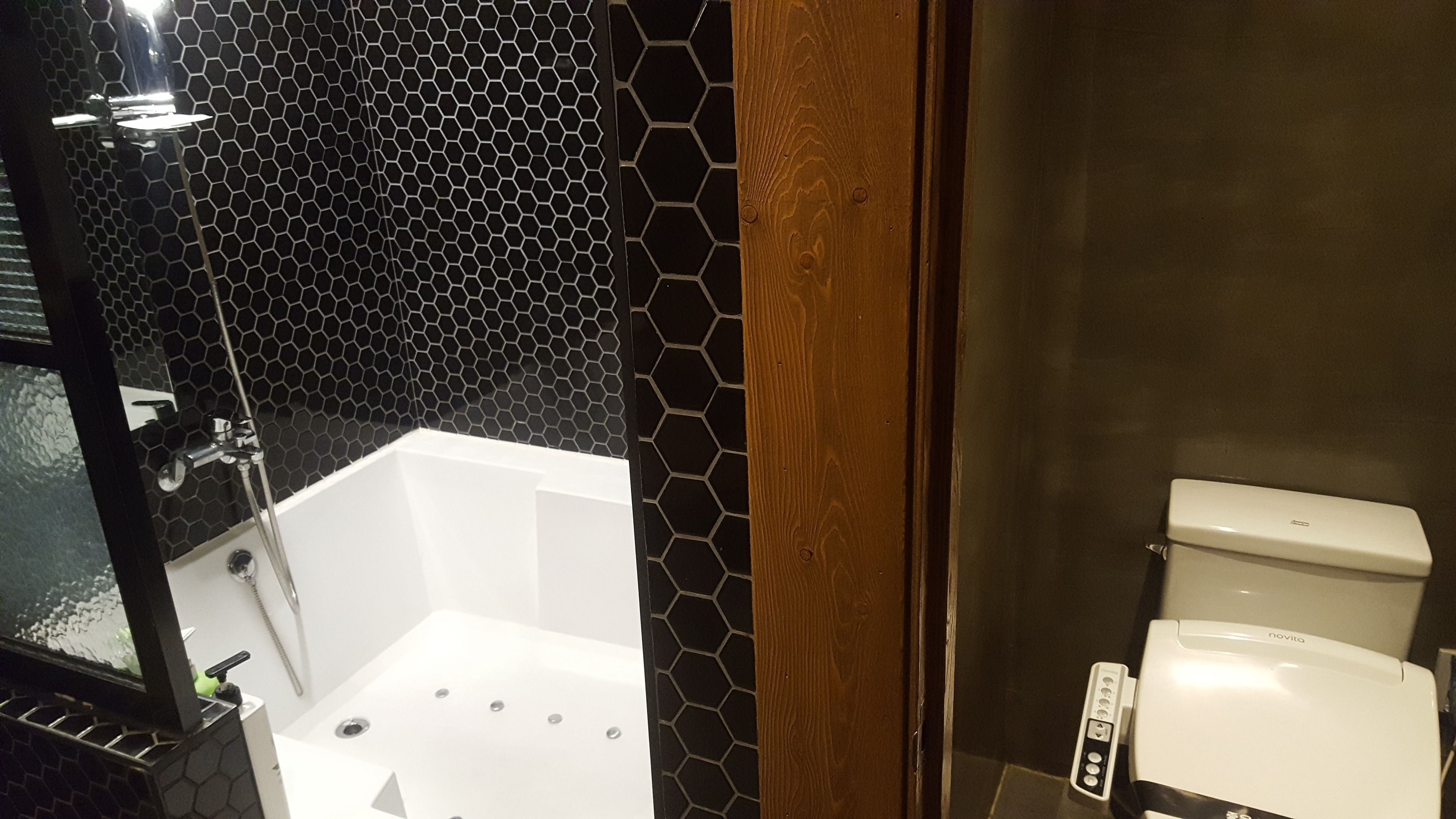 Une salle de bain avec une baignoire blanche, des toilettes et un espace douche avec un mur recouvert de carreaux hexagonaux noirs.