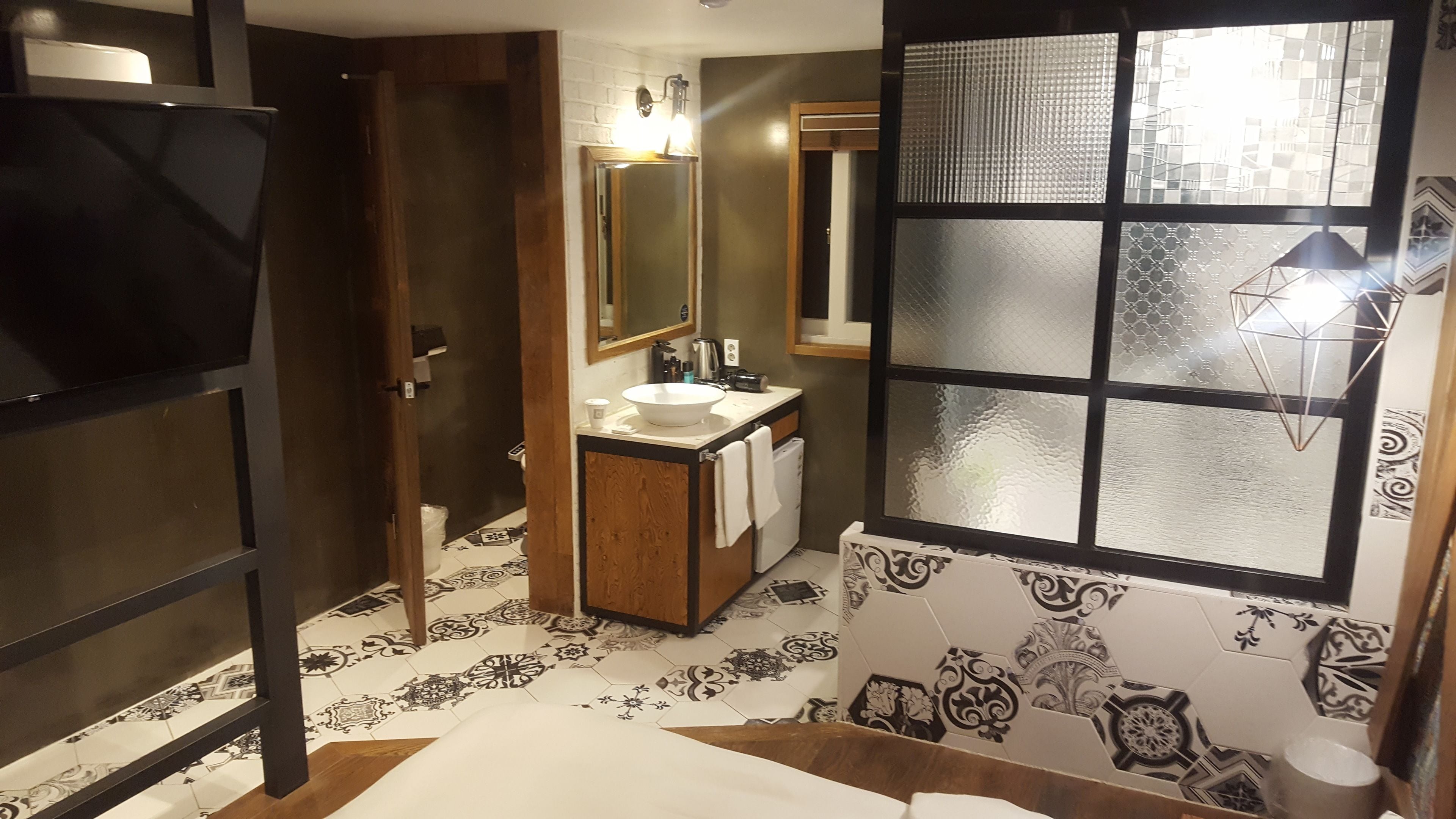 A bathroom with a large mirror, a sink, and a window with frosted glass panels.