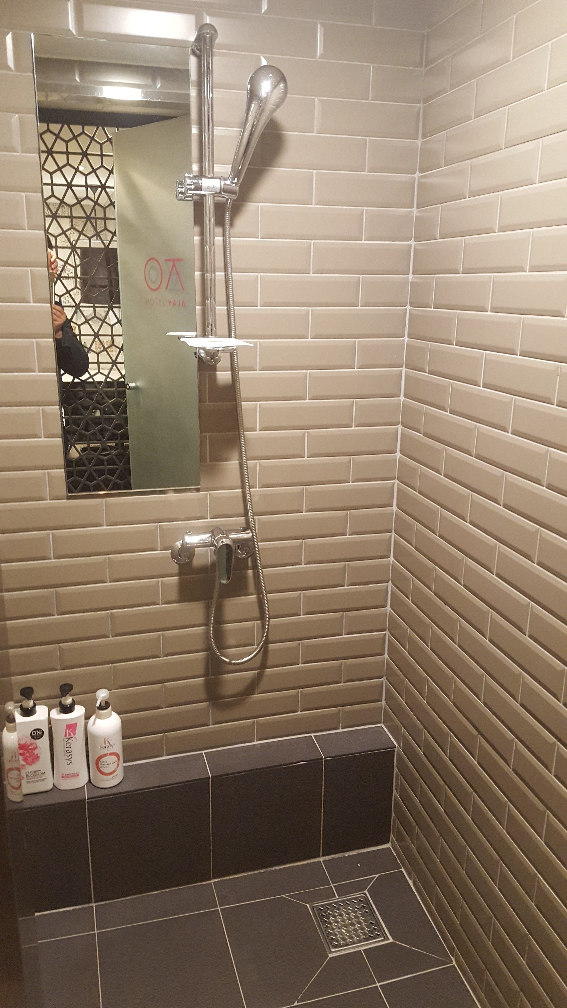 Douchegedeelte met een glazen deur, een metalen douchekop en drie flessen shampoo op de vloer.