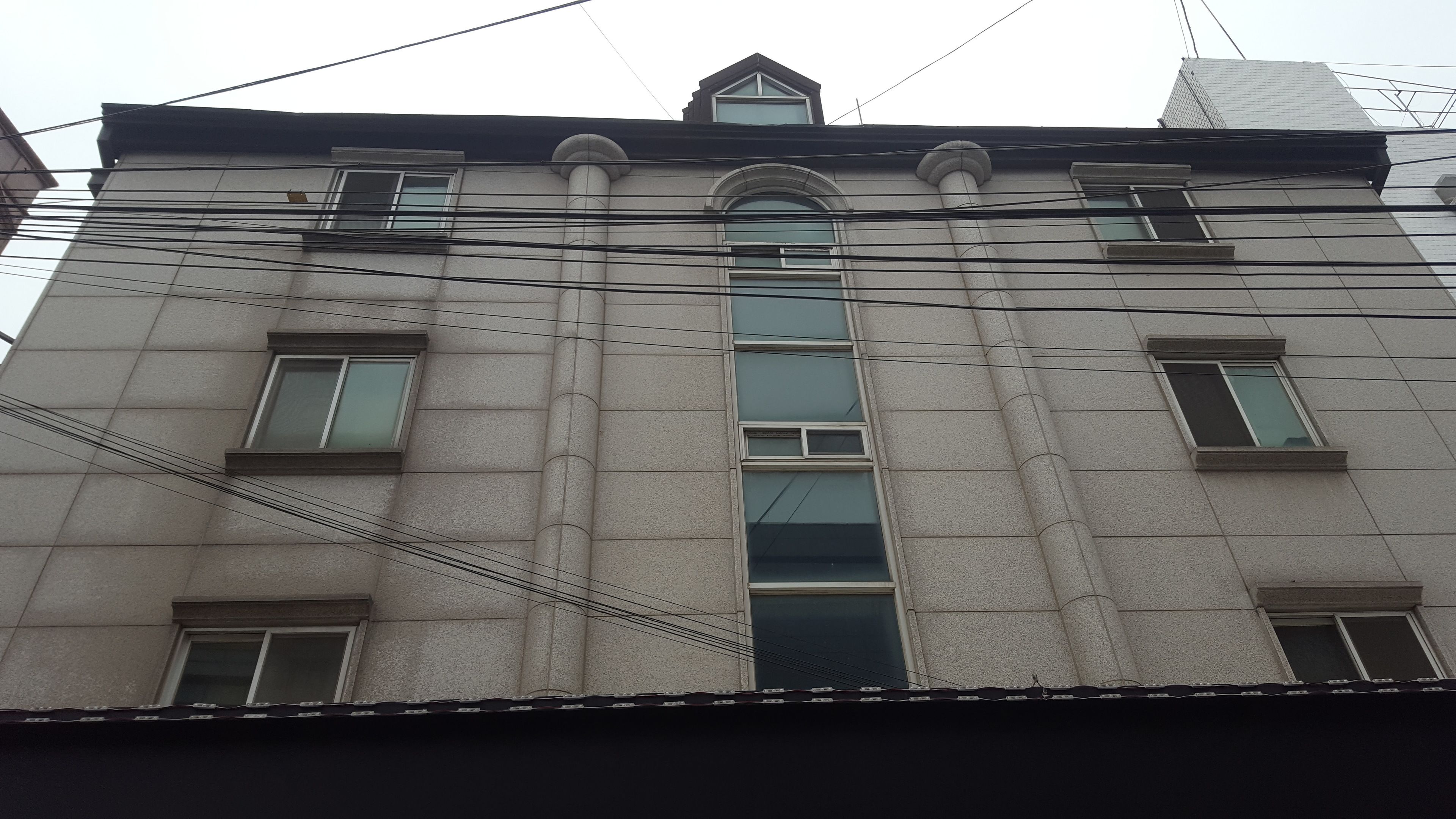 A building with multiple windows and a central arched window. Power lines are visible across the building.