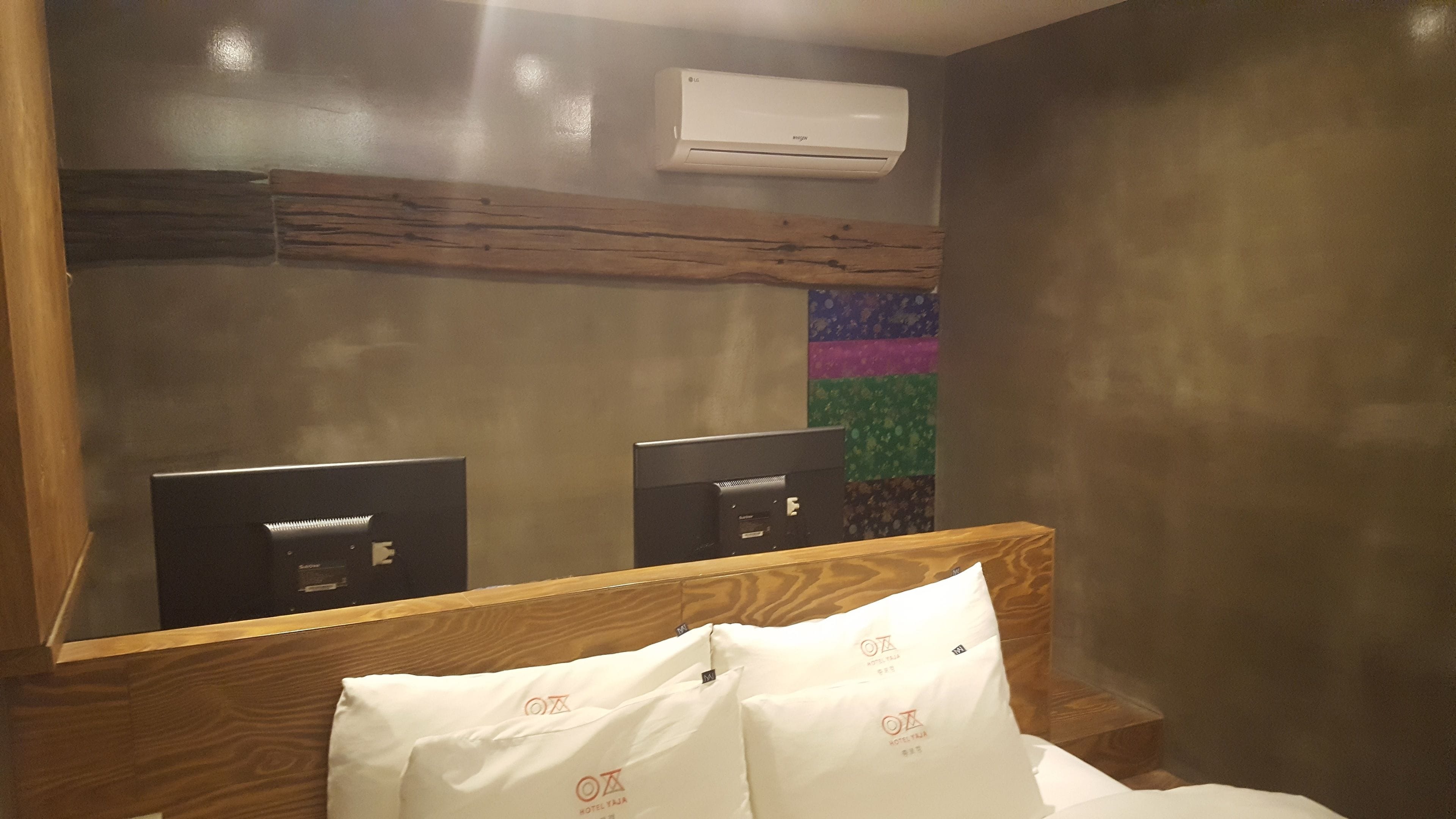 Habitación de hotel con cabecera de madera, un espejo grande y un equipo de aire acondicionado en la pared.
