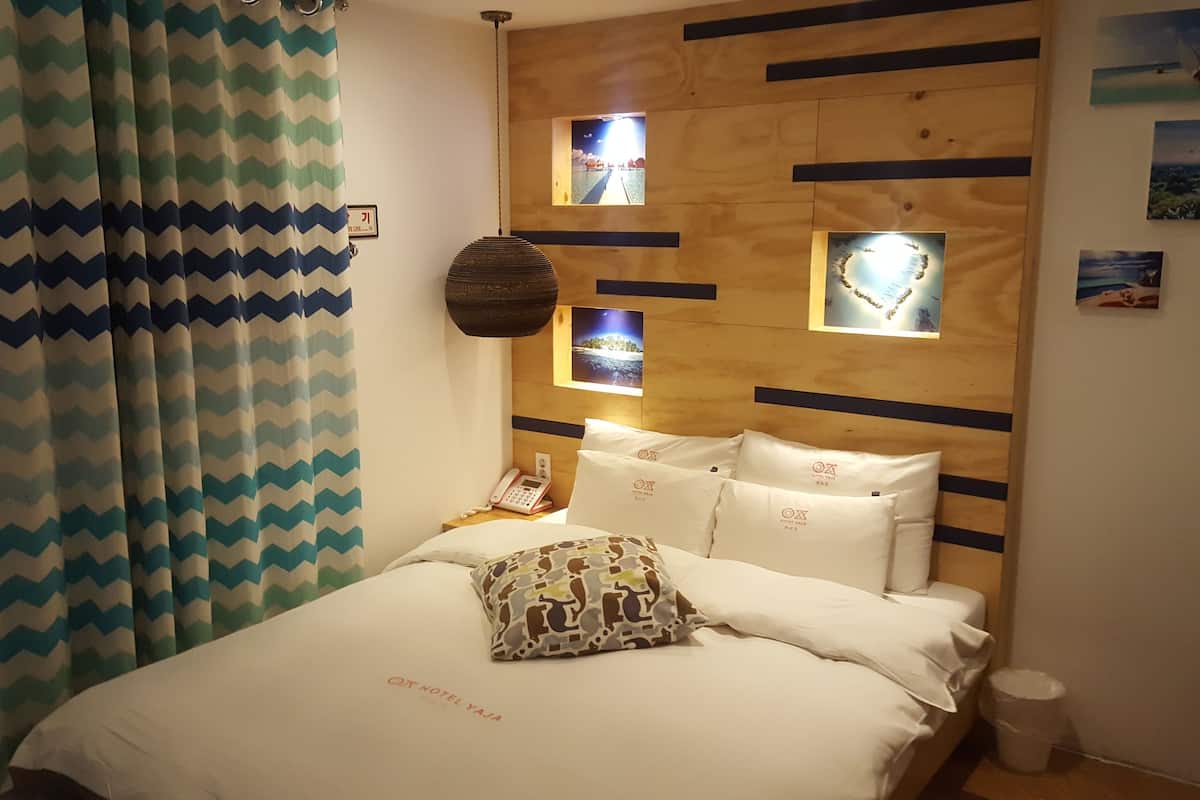 Une chambre d’hôtel avec un lit, une tête de lit en bois et une vue sur la mer par la fenêtre.